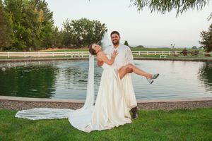 Wedding couple shares a fun moment as groom lifts bride by fountain in garden setting.
