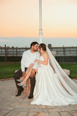 Romantic wedding couple shares intimate moments at sunset on a stone patio near a rustic fence.