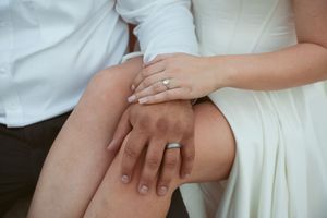 Close up of hands with wedding rings resting on white satin wedding dress fabric.
