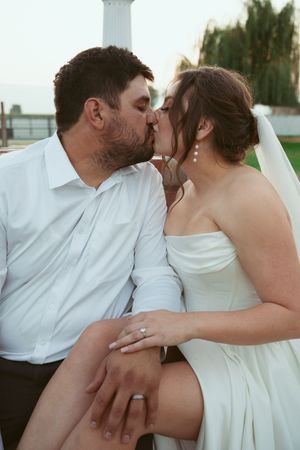 A romantic wedding moment captured outdoors with the couple sharing a kiss while wearing white attire.