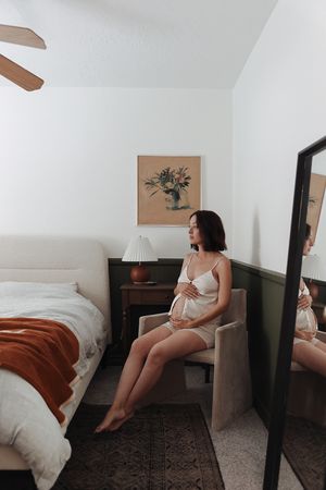 Maternity photo in cozy bedroom setting with soft decor and natural lighting.