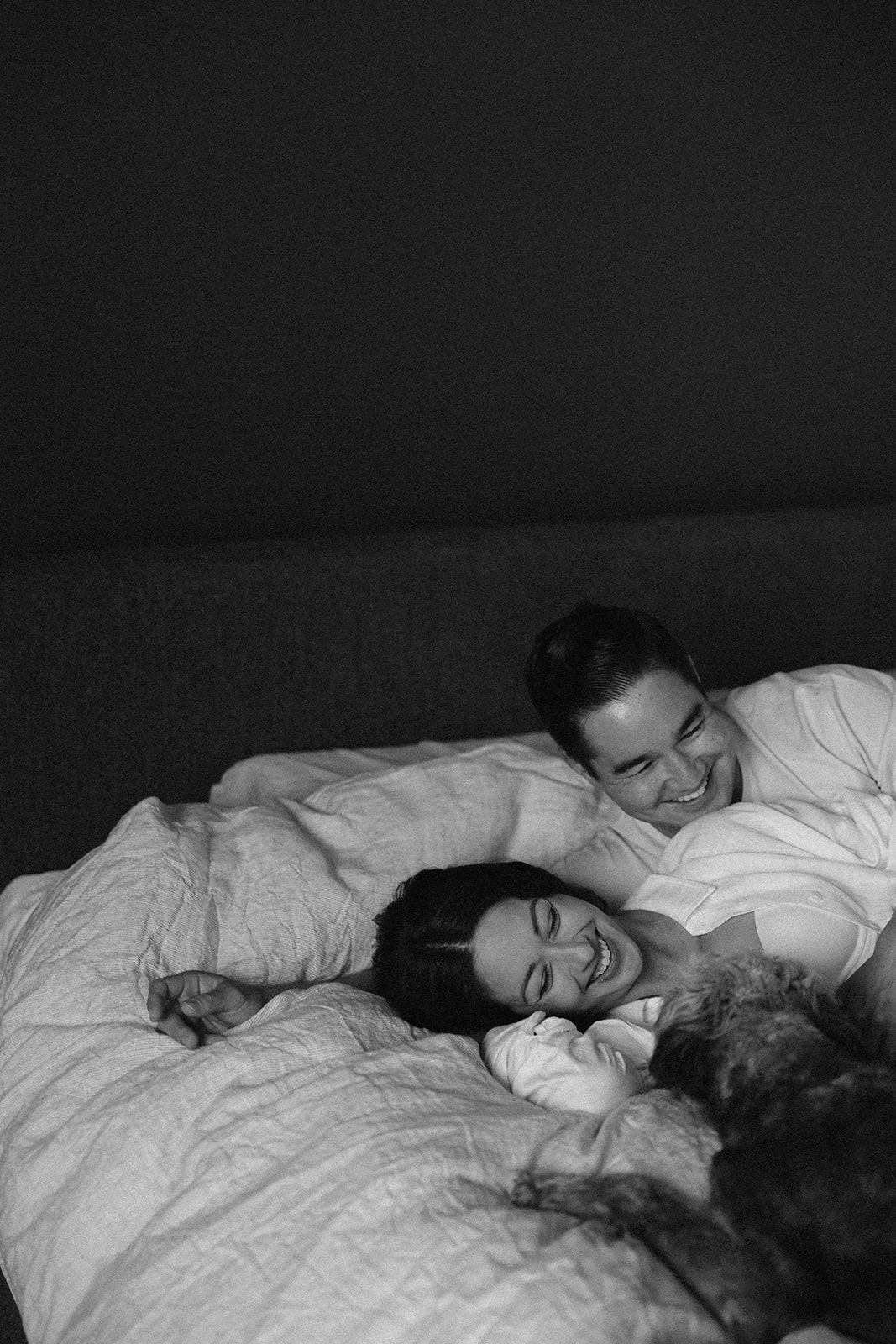 Black and white intimate bedroom photo of couple with pet sharing joyful moment.