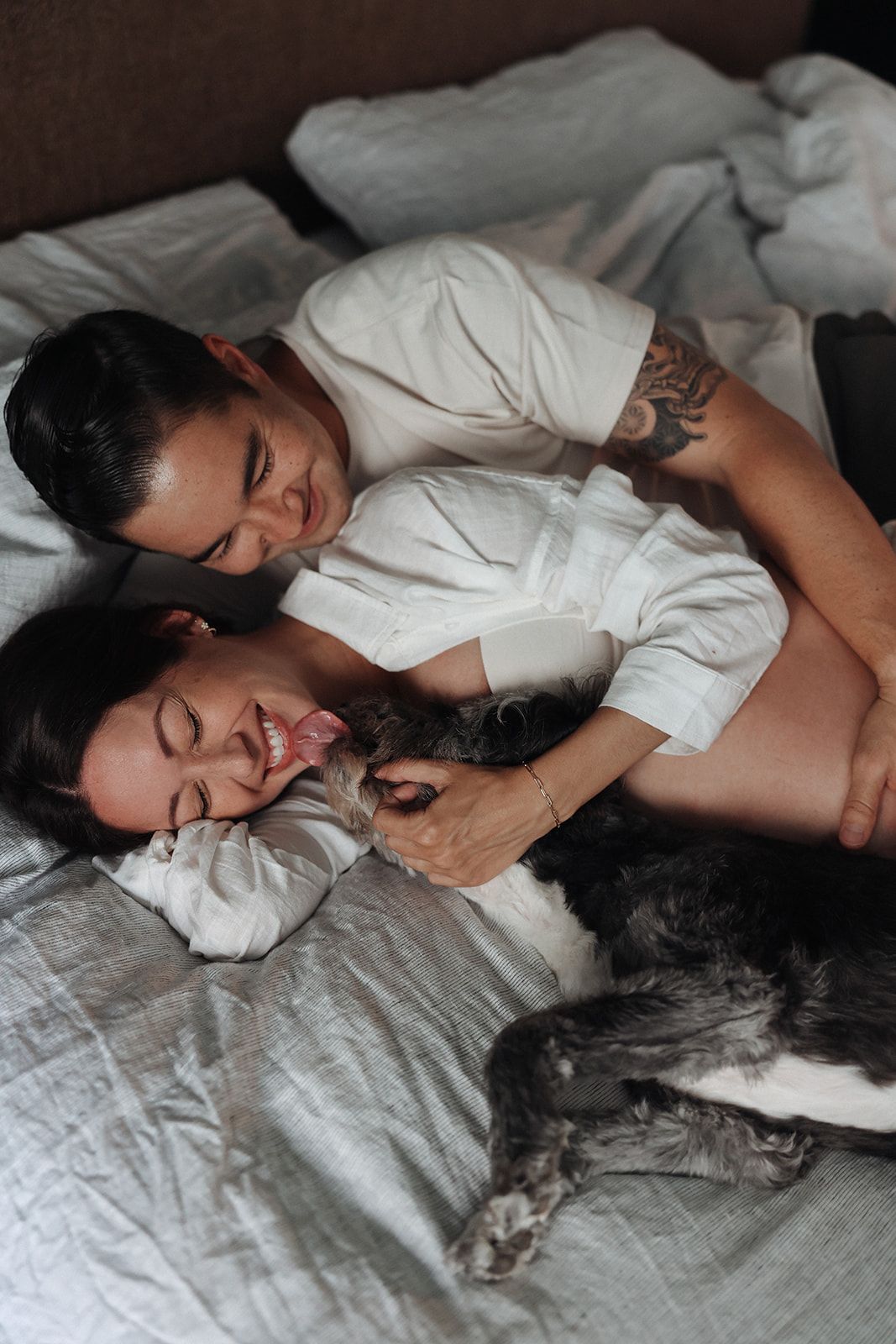Couple relaxing on bed with cat in casual white attire during intimate photoshoot.