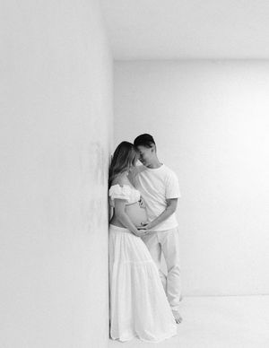 Black and white photo of an intimate moment between a couple embracing against a white wall in minimalist setting.