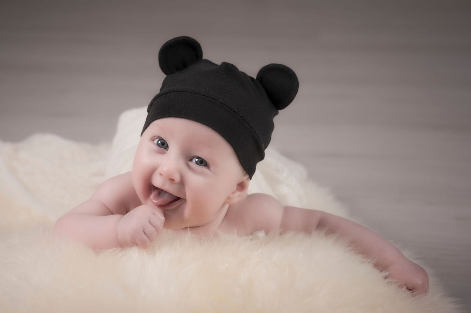 Baby wearing black beanie hat lying on pink blanket.