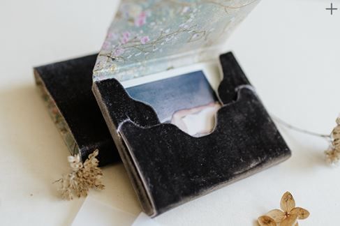 A vintage black leather cardholder with small gold flower decorations beside it on a white surface.