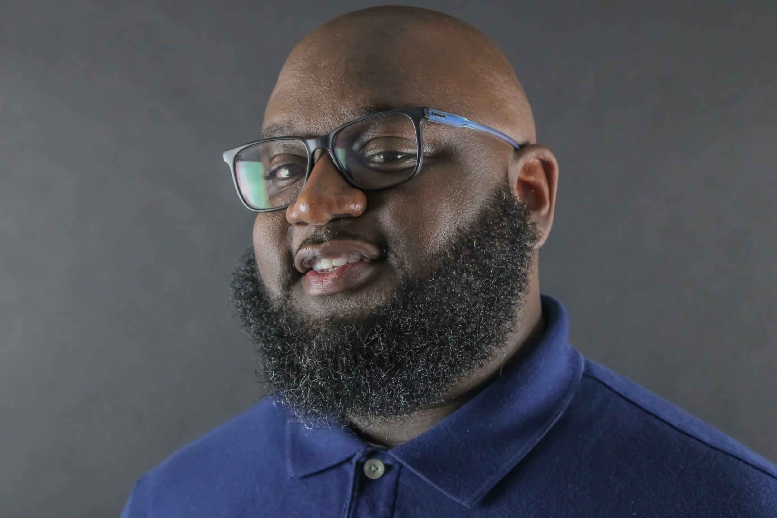 Professional headshot of a person wearing glasses and blue polo shirt against grey background.