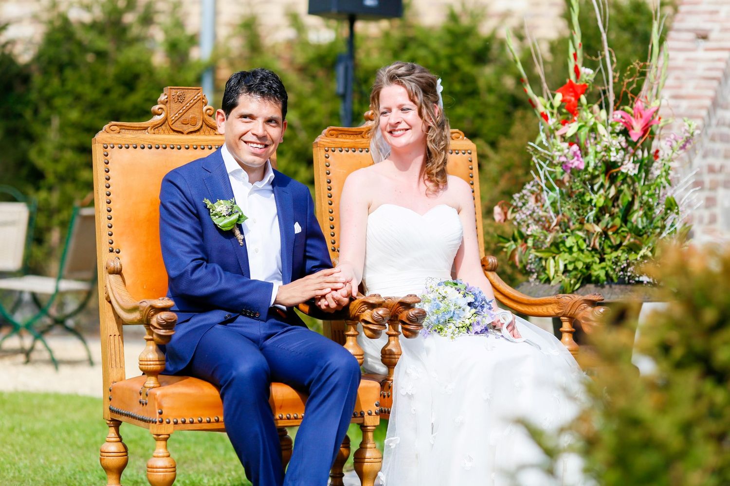 A couple holds hands during an intimate wedding ceremony with wine barrels and floral arrangements in the background.