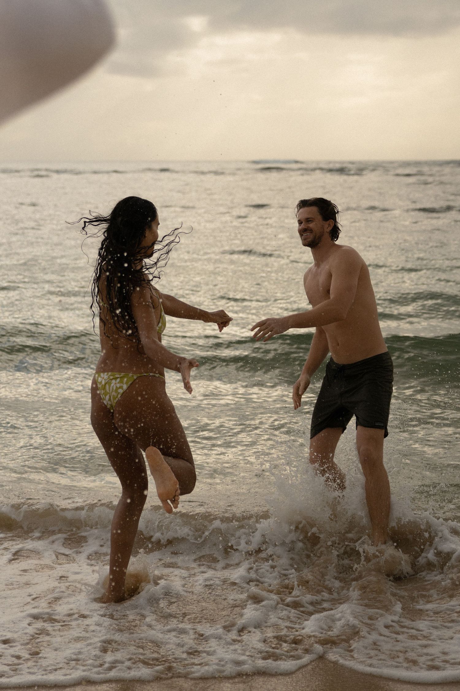 A playful couple splashing in ocean waves during sunset.