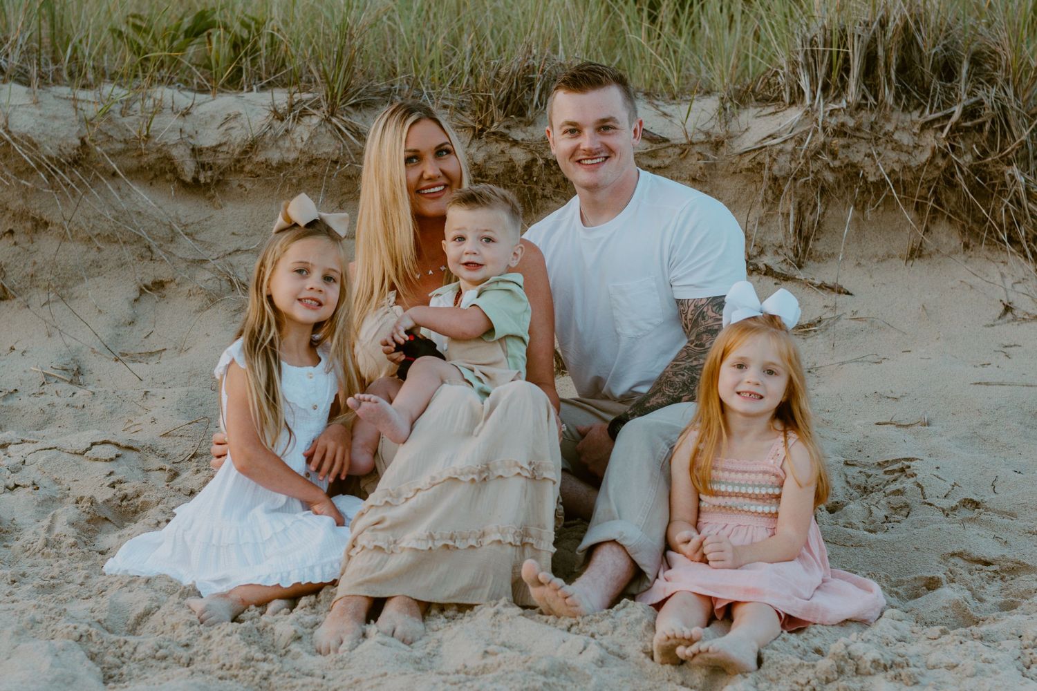 A family sits together on a sandy beach during golden hour for a casual outdoor portrait session.