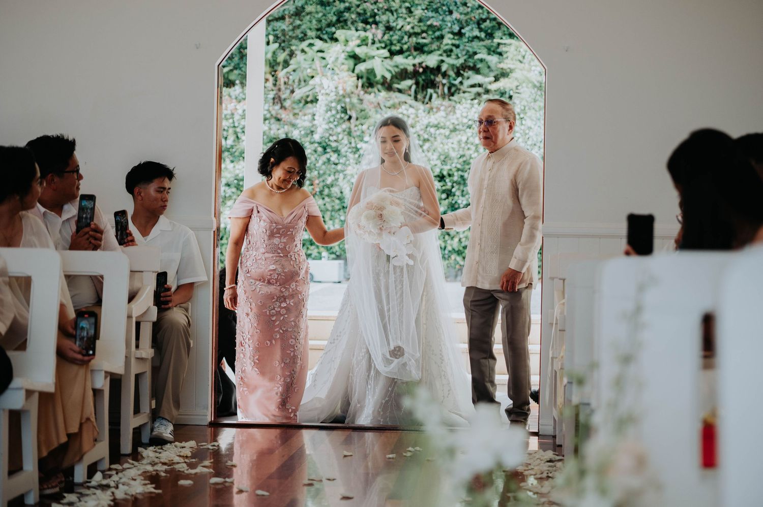 Wedding ceremony taking place under an elegant white archway with attendees in formal attire.