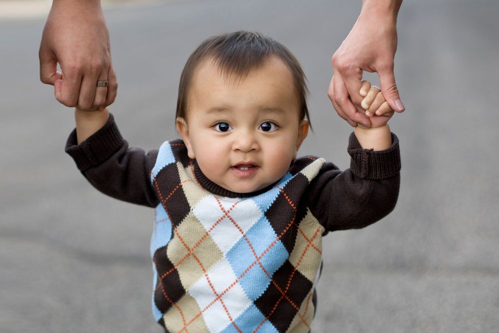 Portrait of baby looking at camera while holding their parents hands