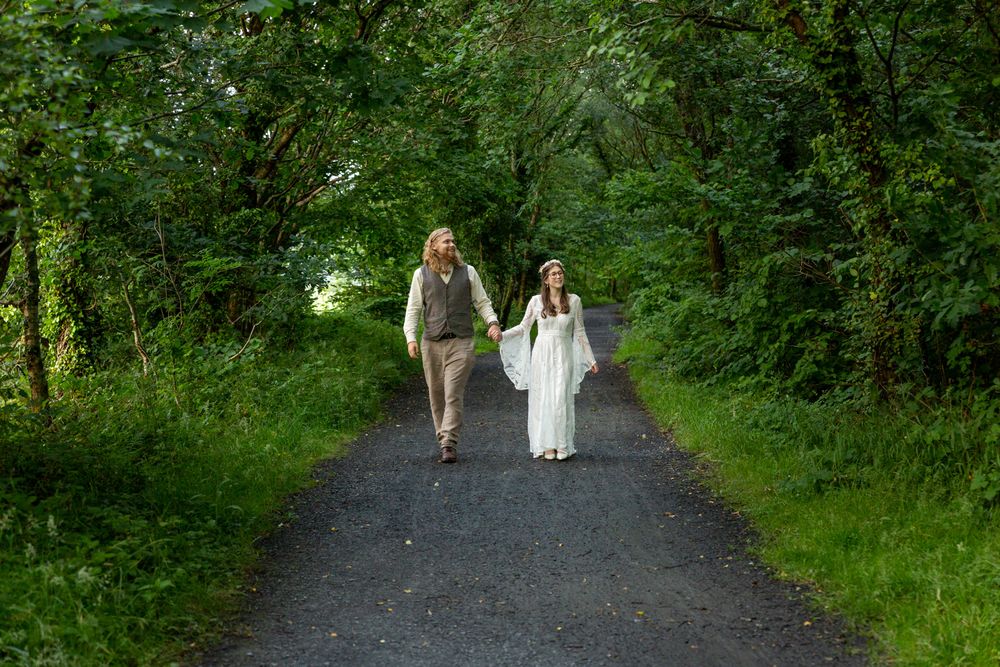A wedding portrait of a bride and groom walking along a woodland path while holding hands.