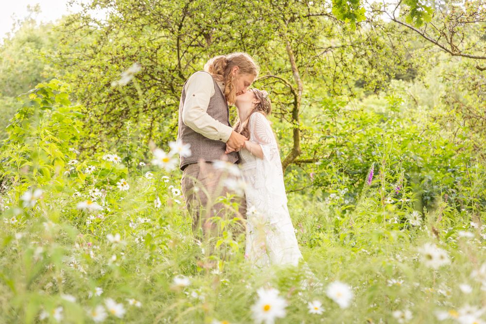 A colourful wedding portrait of a couple kissing amongst wild flowers in a woodland glade.
