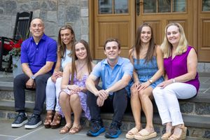 A family group sits together on outdoor stone steps in coordinated casual outfits for a professional photo session.