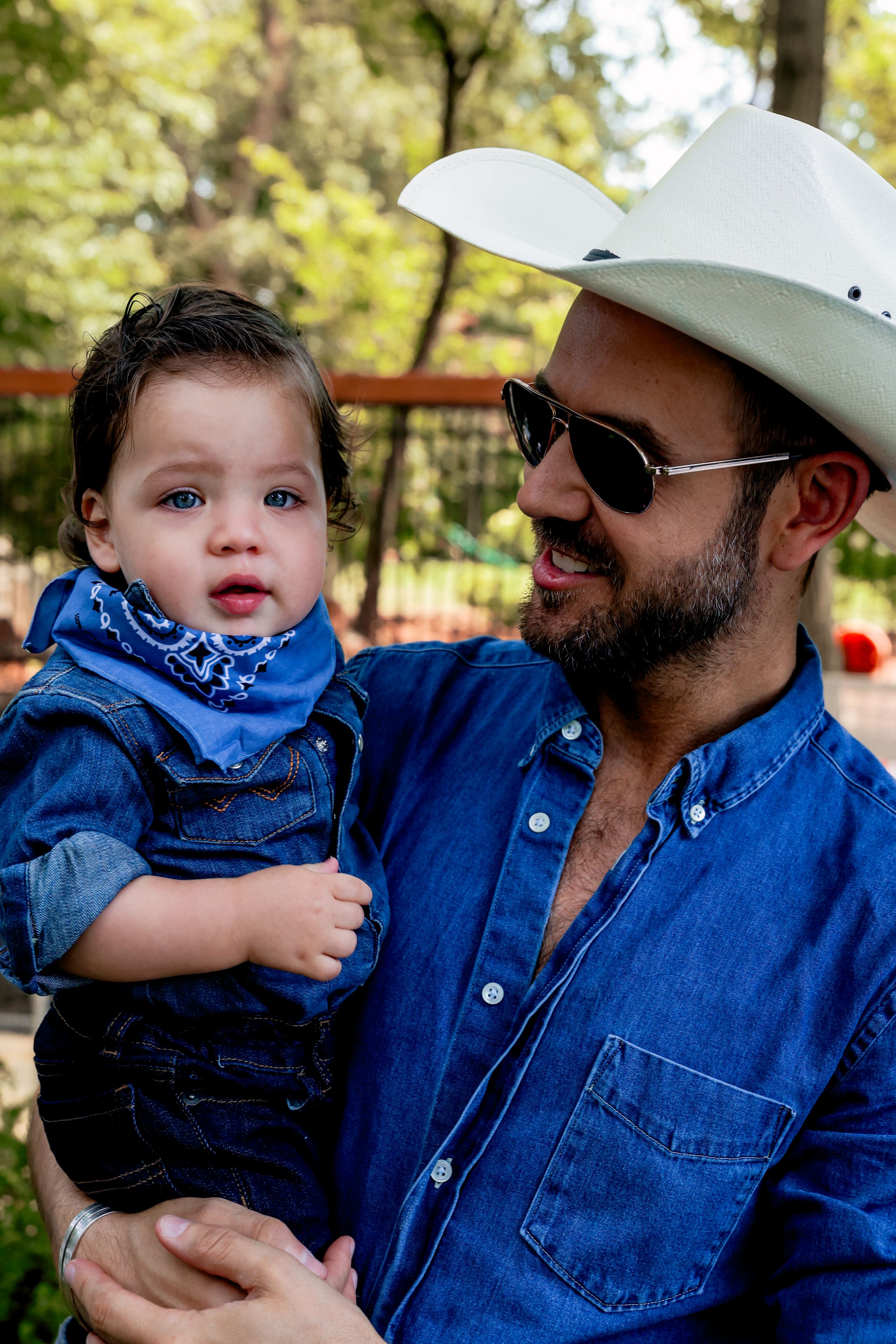 Parent and child in matching denim outfits enjoy a sunny day in the park, with white cowboy hat and blue bandana.