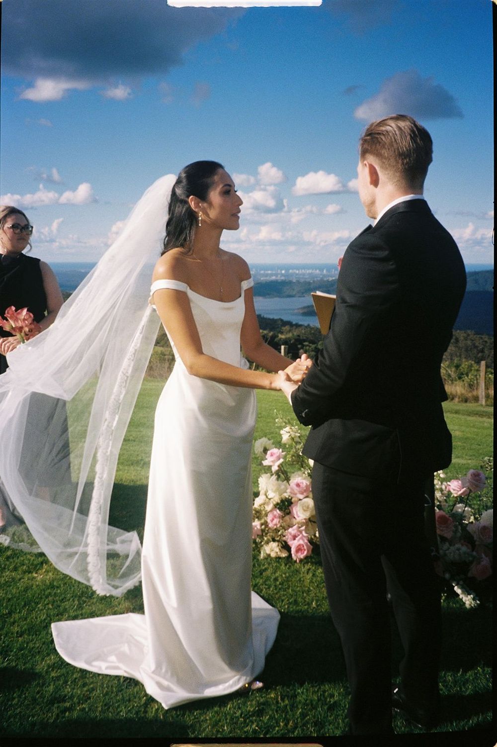 A sequence of four wedding photos showing a couple embracing outdoors with a scenic ocean view and flowing veil in the breeze.