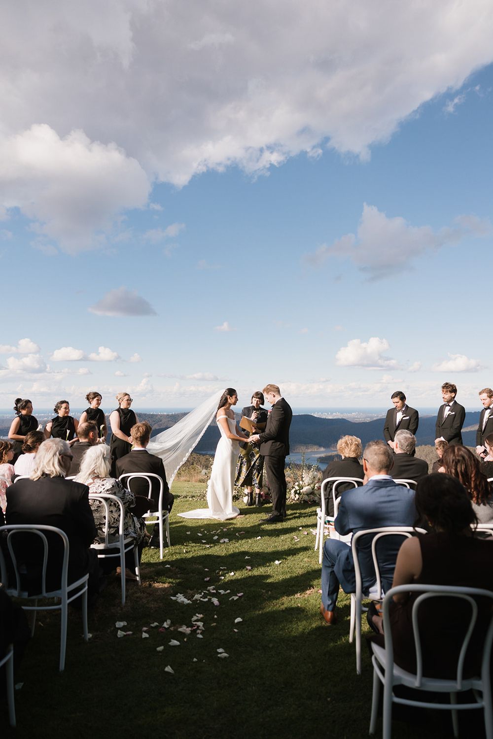 An outdoor wedding ceremony on a mountain summit with white chairs and scattered flower petals along the aisle.