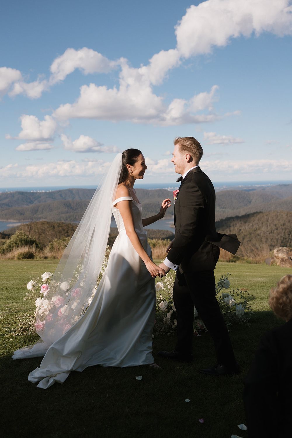 A couple shares an intimate moment on a hilltop overlooking a scenic mountain landscape on their wedding day.