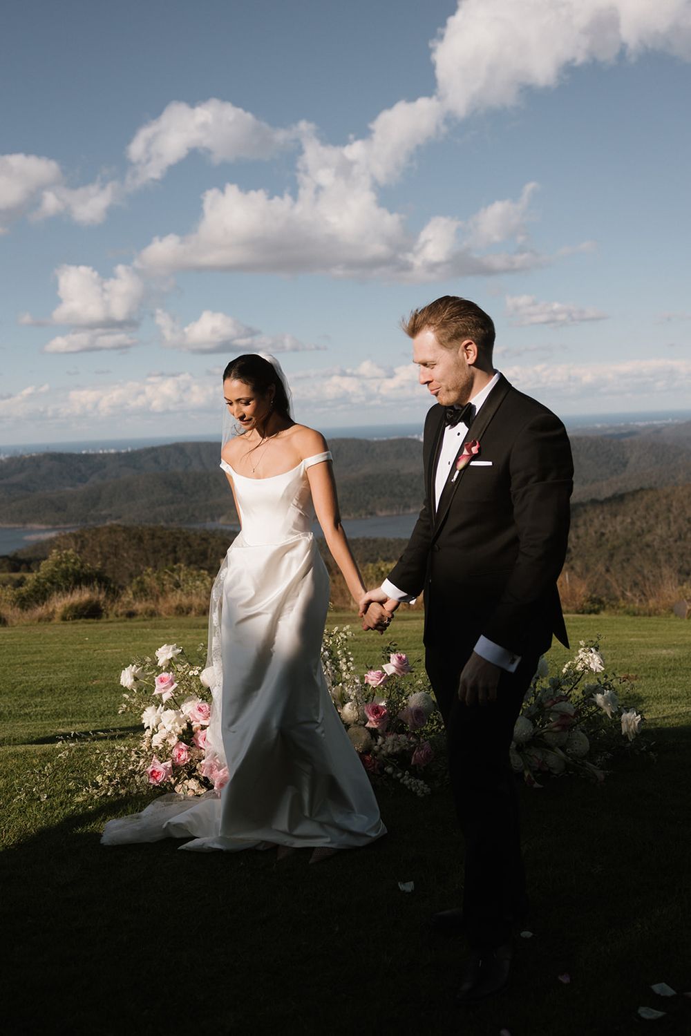A couple shares a romantic moment on a hilltop meadow with mountain views and floral arrangements on a cloudy day.