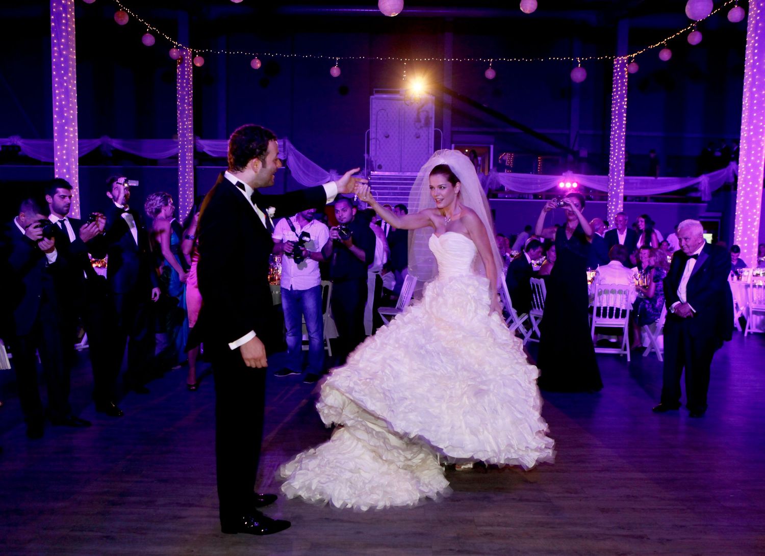 Glowing lights illuminate a wedding reception dance floor where a bride in a white dress twirls gracefully.