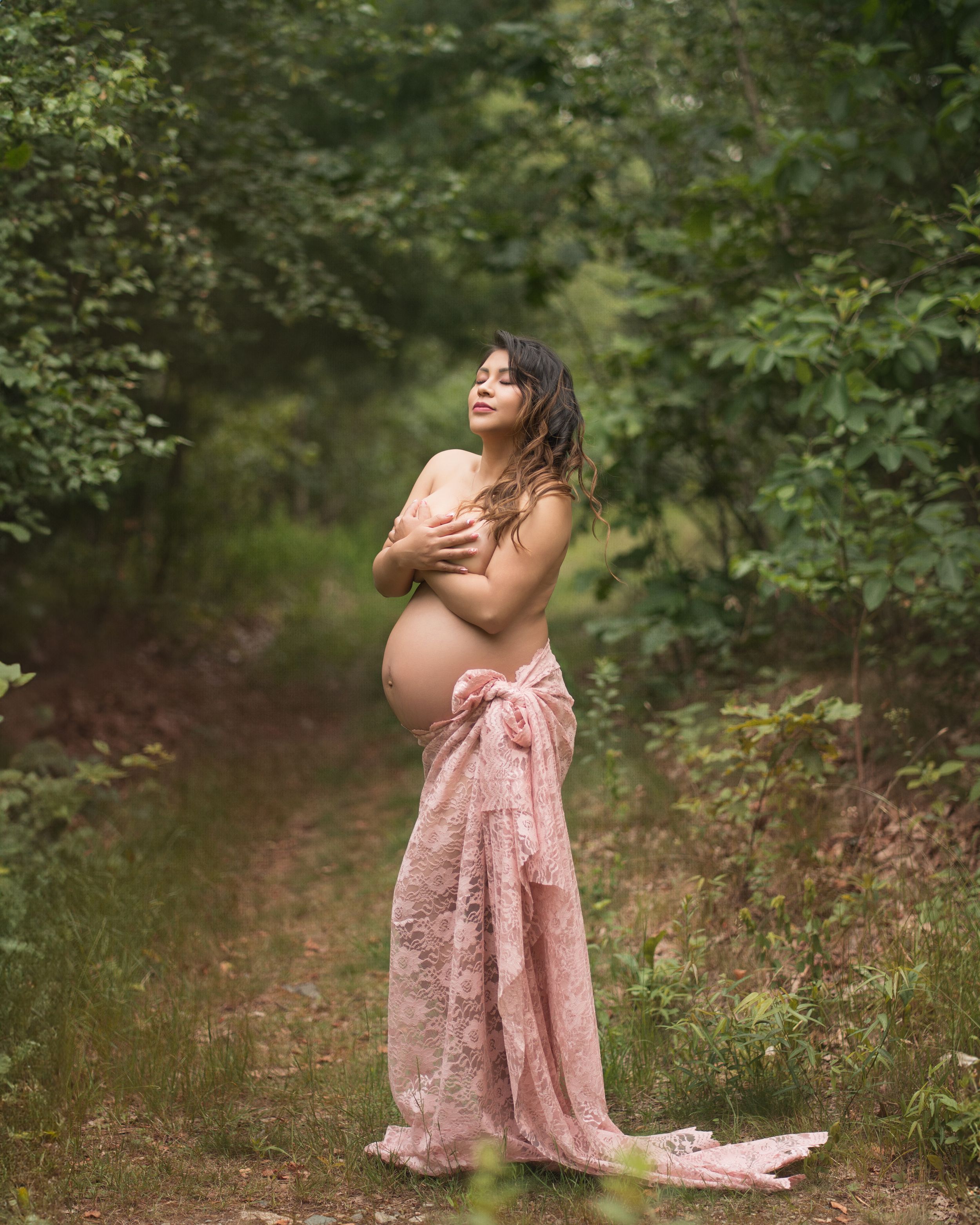 Artistic maternity photo in nature featuring flowing pink lace fabric.