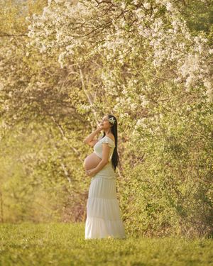 Dreamy maternity photo under spring cherry blossoms in white dress.