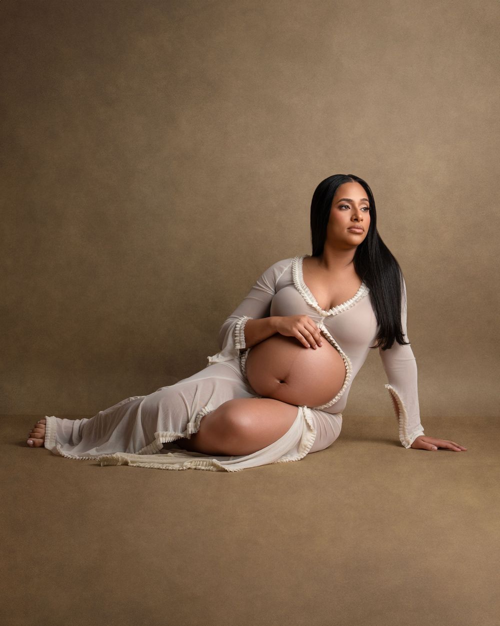 Maternity portrait featuring an elegant white dress and natural pose against neutral backdrop.