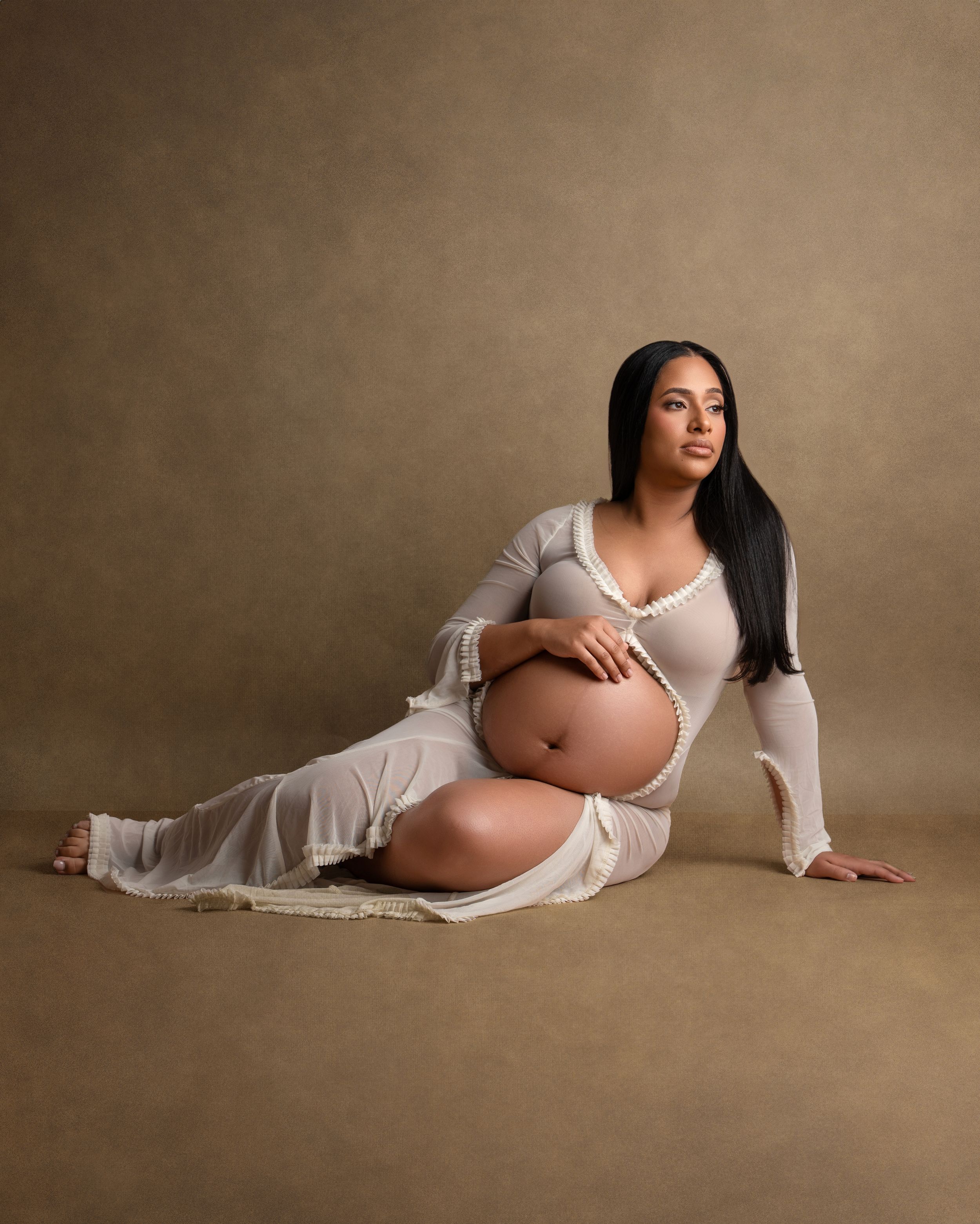 Maternity portrait featuring an elegant white dress and natural pose against neutral backdrop.