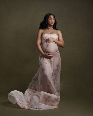 Maternity portrait in a flowing pink gown against a dark backdrop showcasing elegant pregnancy photography.