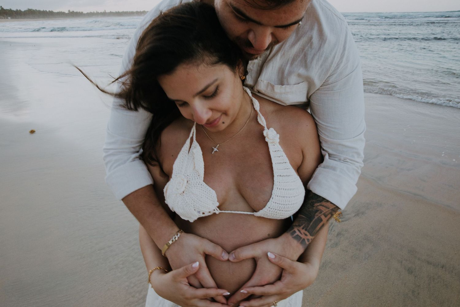 Intimate beach photoshoot of a couple embracing on the sand with ocean waves in the background.