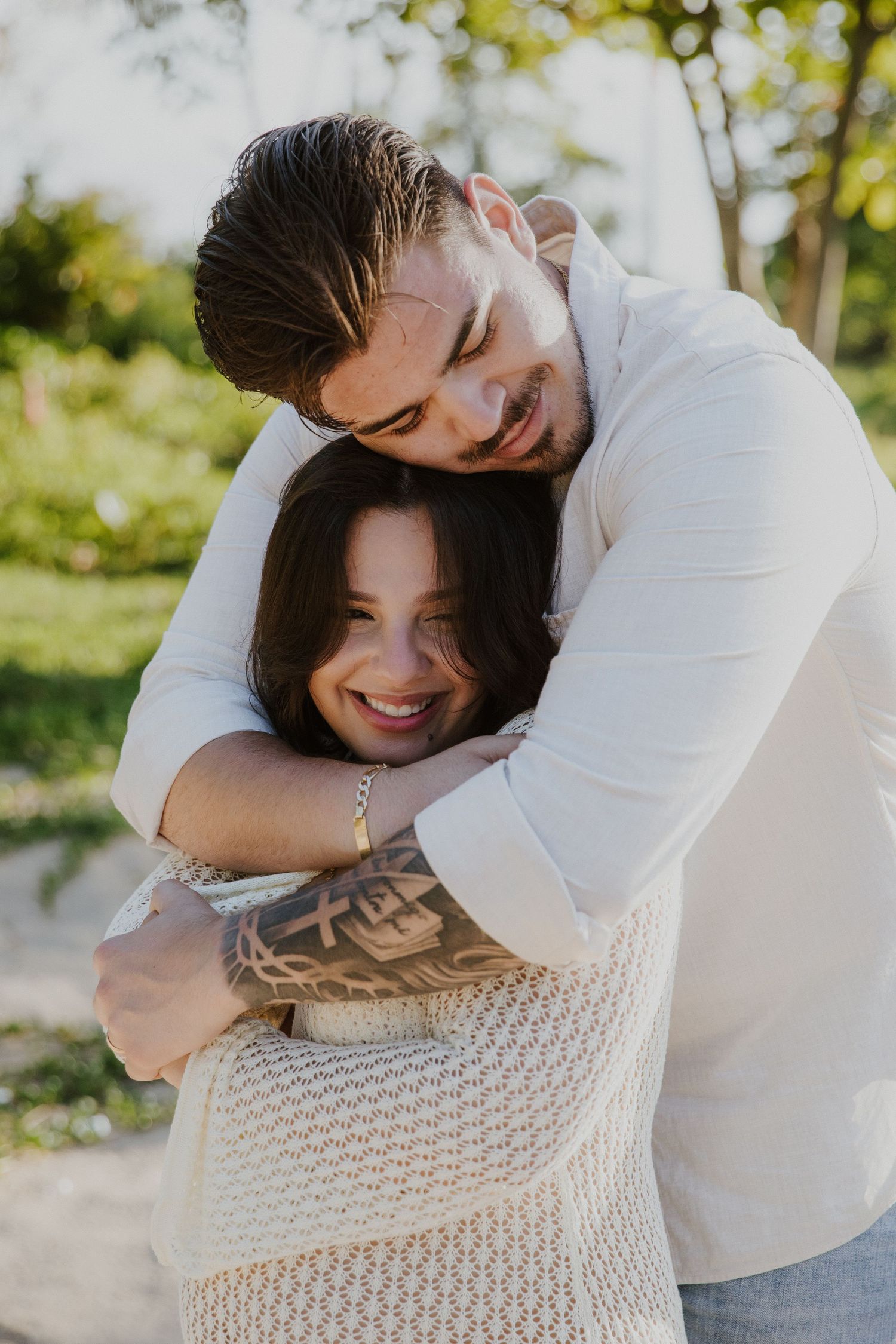 A romantic couple embracing outdoors in warm sunlight with palm trees in the background.