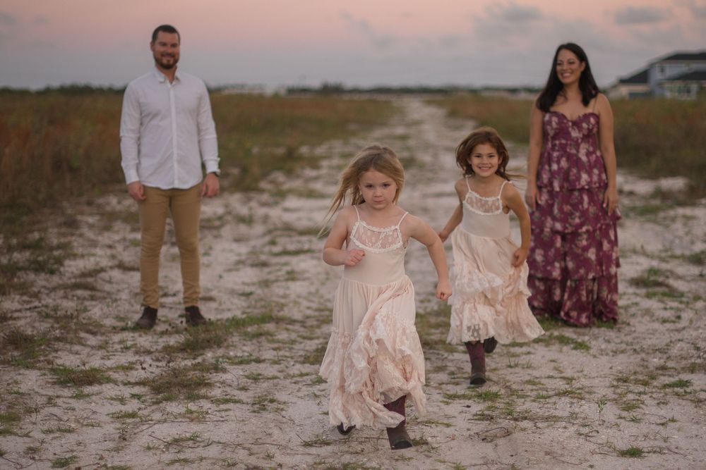 A group of people walk and pose together along a sandy beach at sunset with a peaceful coastal backdrop.