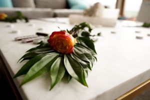 Single orange rose with green leaves artistically arranged on a white surface.