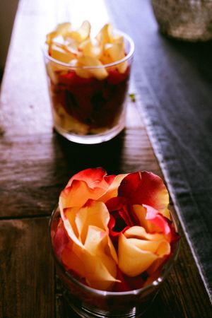 Orange roses in a glass vase next to a dark beverage on a wooden surface.
