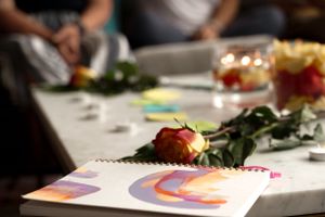 A colorful rainbow artwork and rose lie on a table during a gathering.