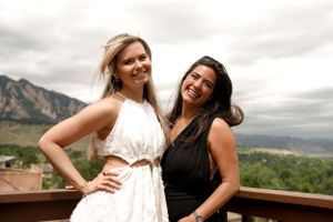 Two friends laughing together on deck with mountain backdrop.
