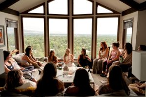 Sunny room with vaulted ceilings and large windows hosting a group circle gathering.