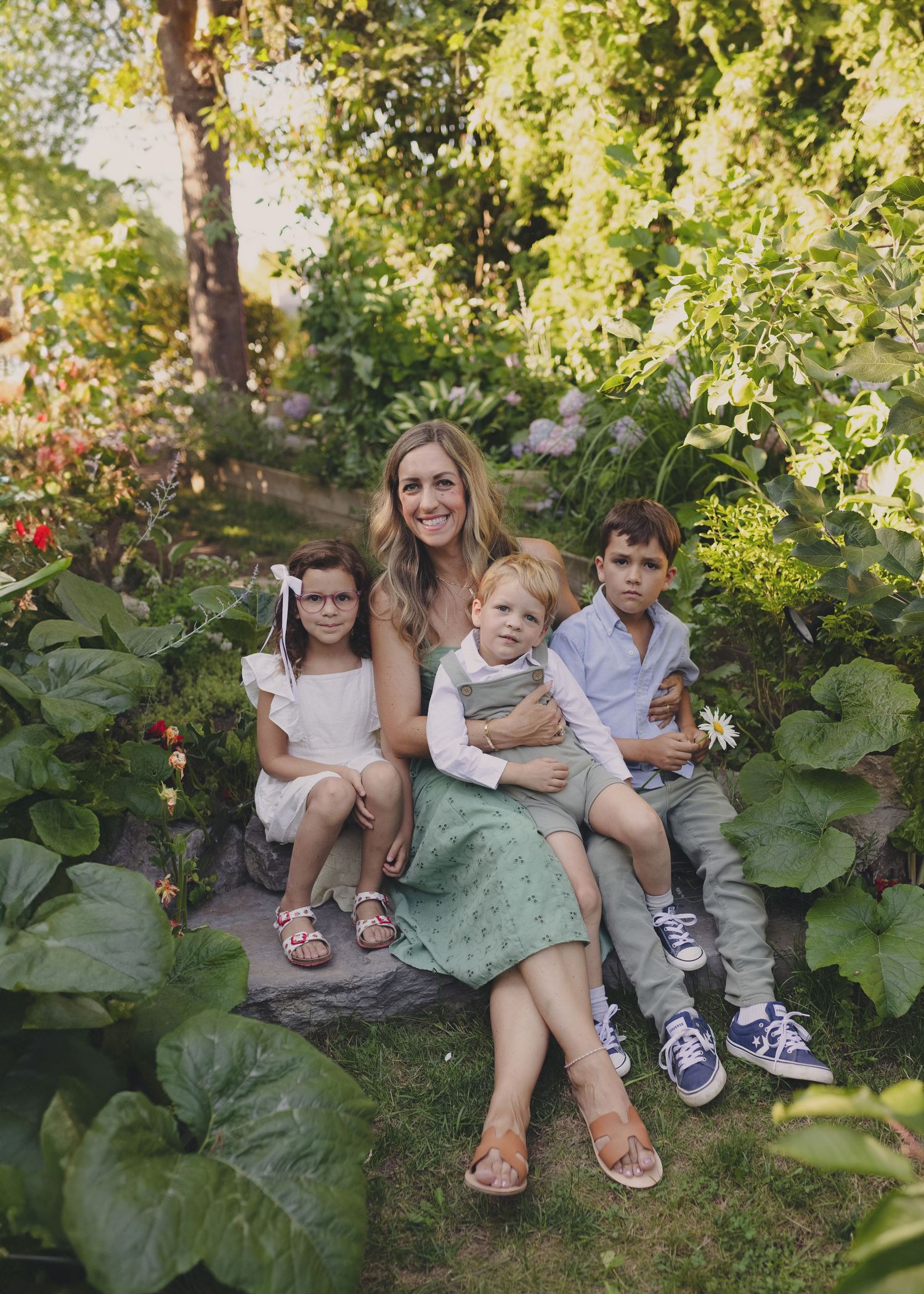 garden mini session Candice and kids sit on a blanket under the trees that glow with summer sunshine