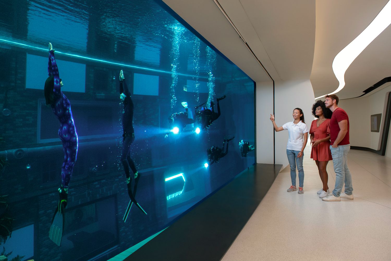 Visitors observe a large interactive digital display wall with glowing blue elements in a modern museum gallery space.