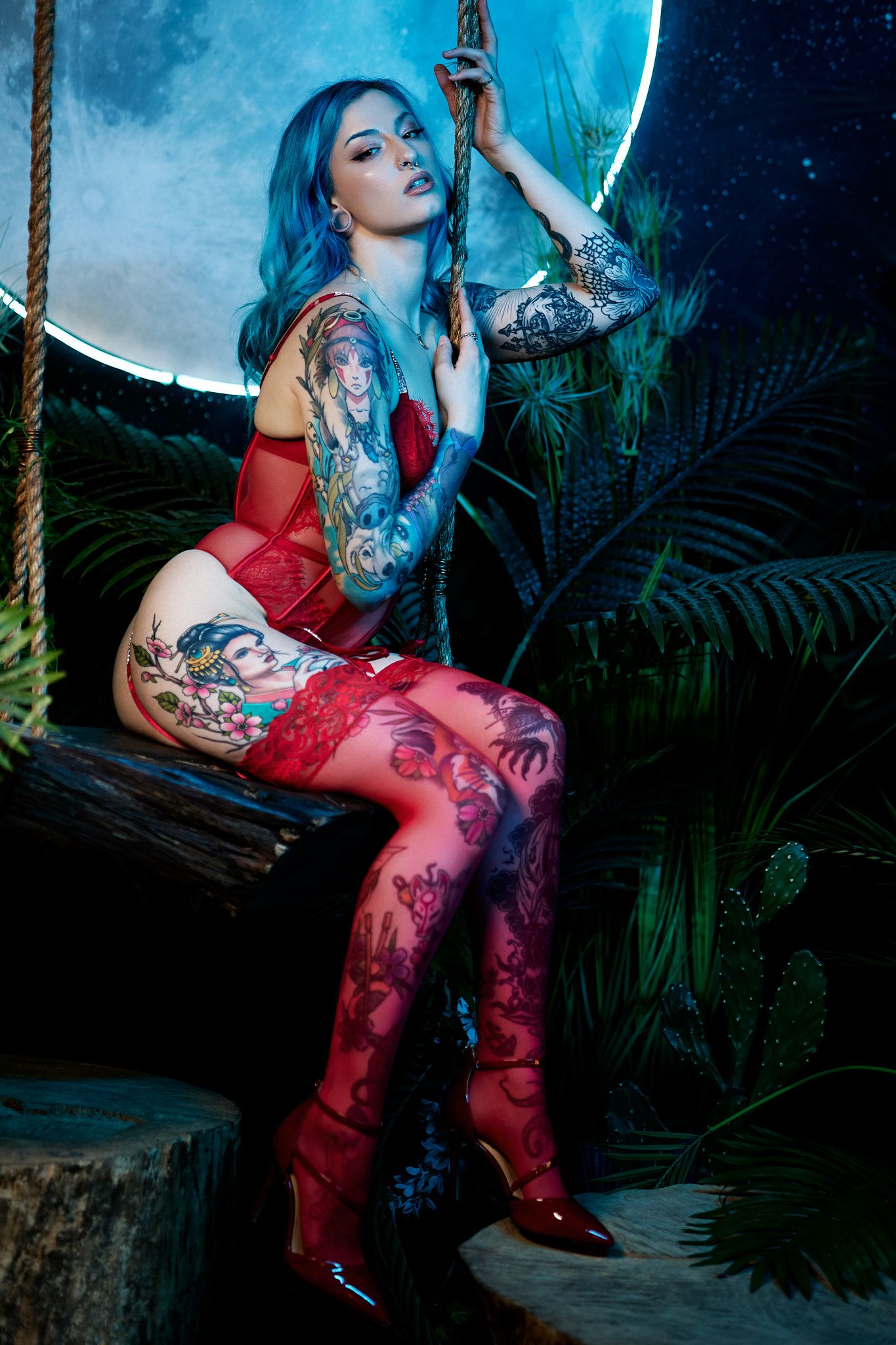 Person in flowing red dress poses dramatically against moody blue-lit tropical garden backdrop.