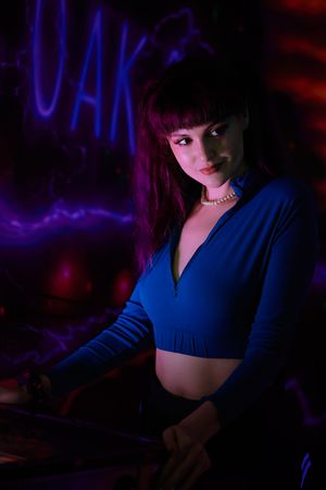 Atmospheric nightclub scene with blue and purple neon lighting illuminating a figure in a cropped navy top.