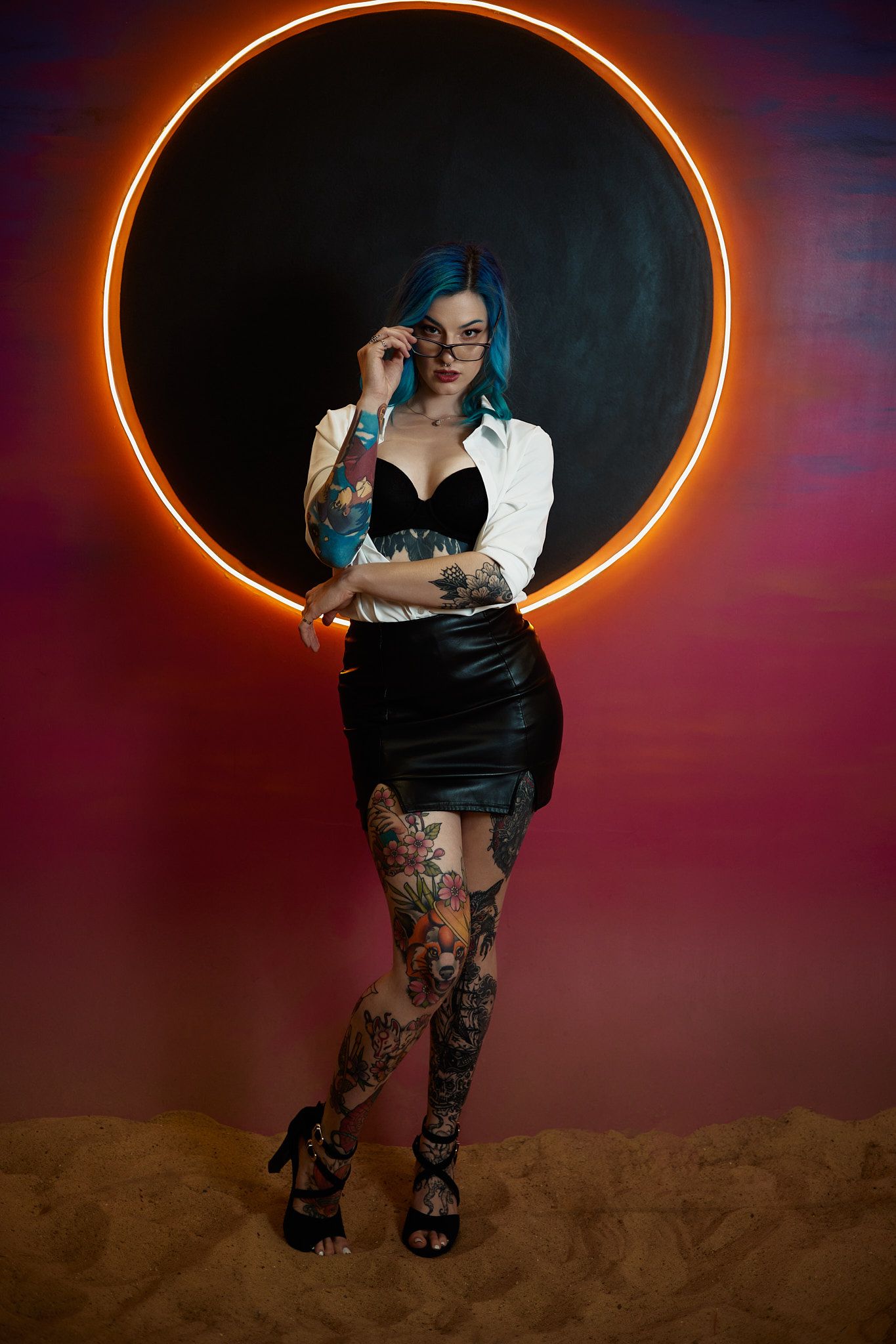 Alternative model in black leather and white shirt poses against glowing orange ring backdrop with artistic lighting.