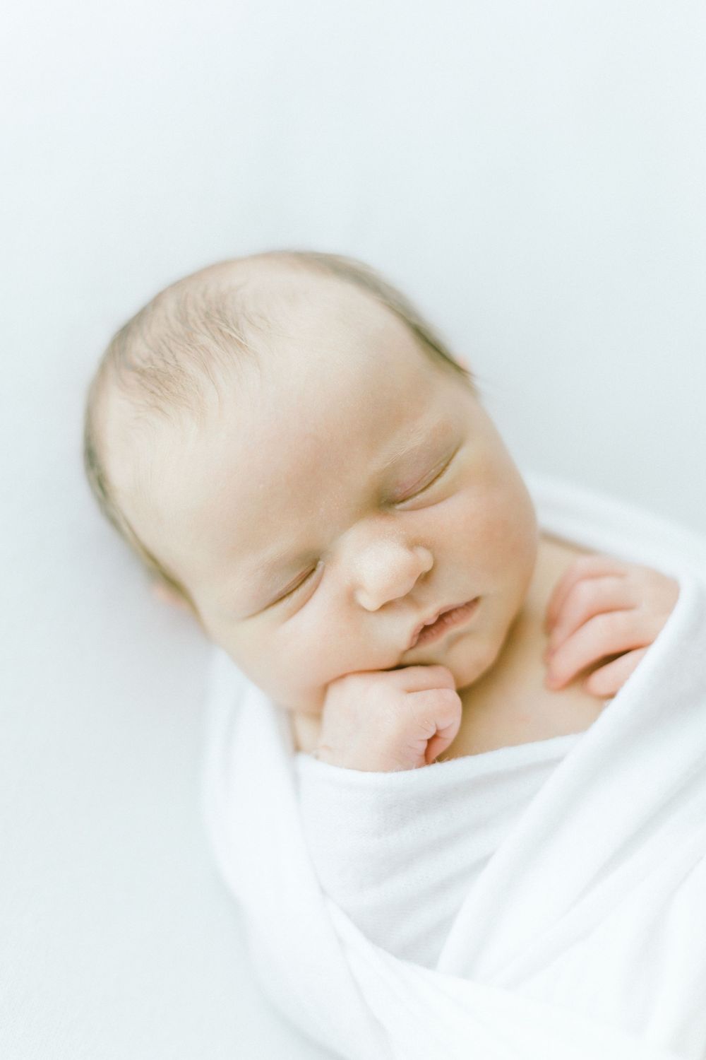 Serene newborn portraits in white swaddle against minimalist background.