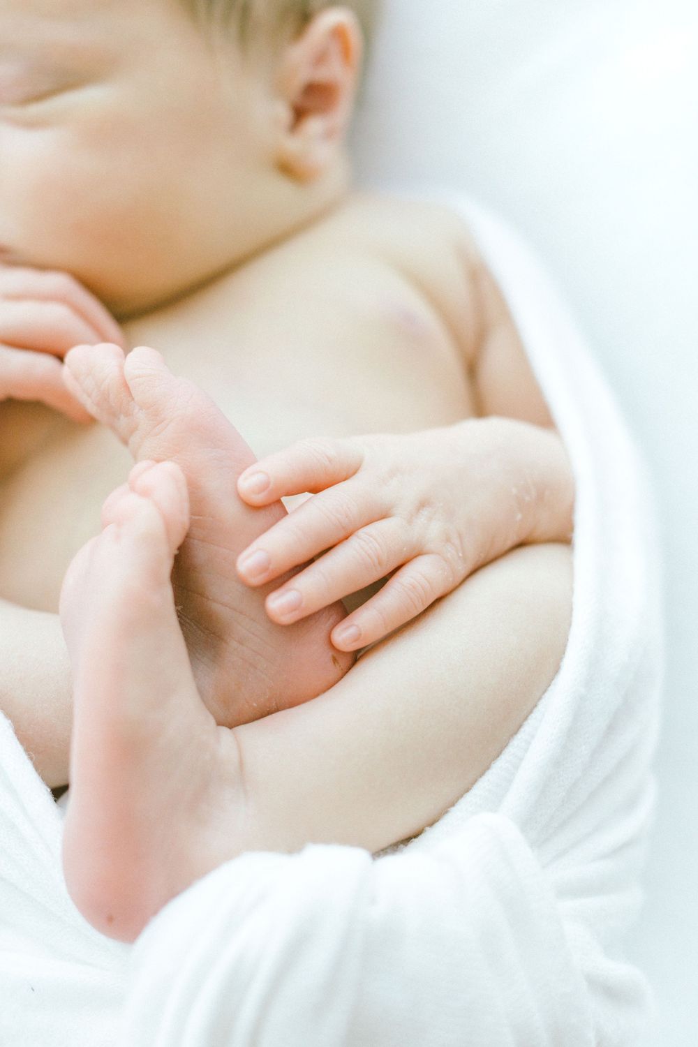 Gentle hands cradling sleeping newborn in white fabric.