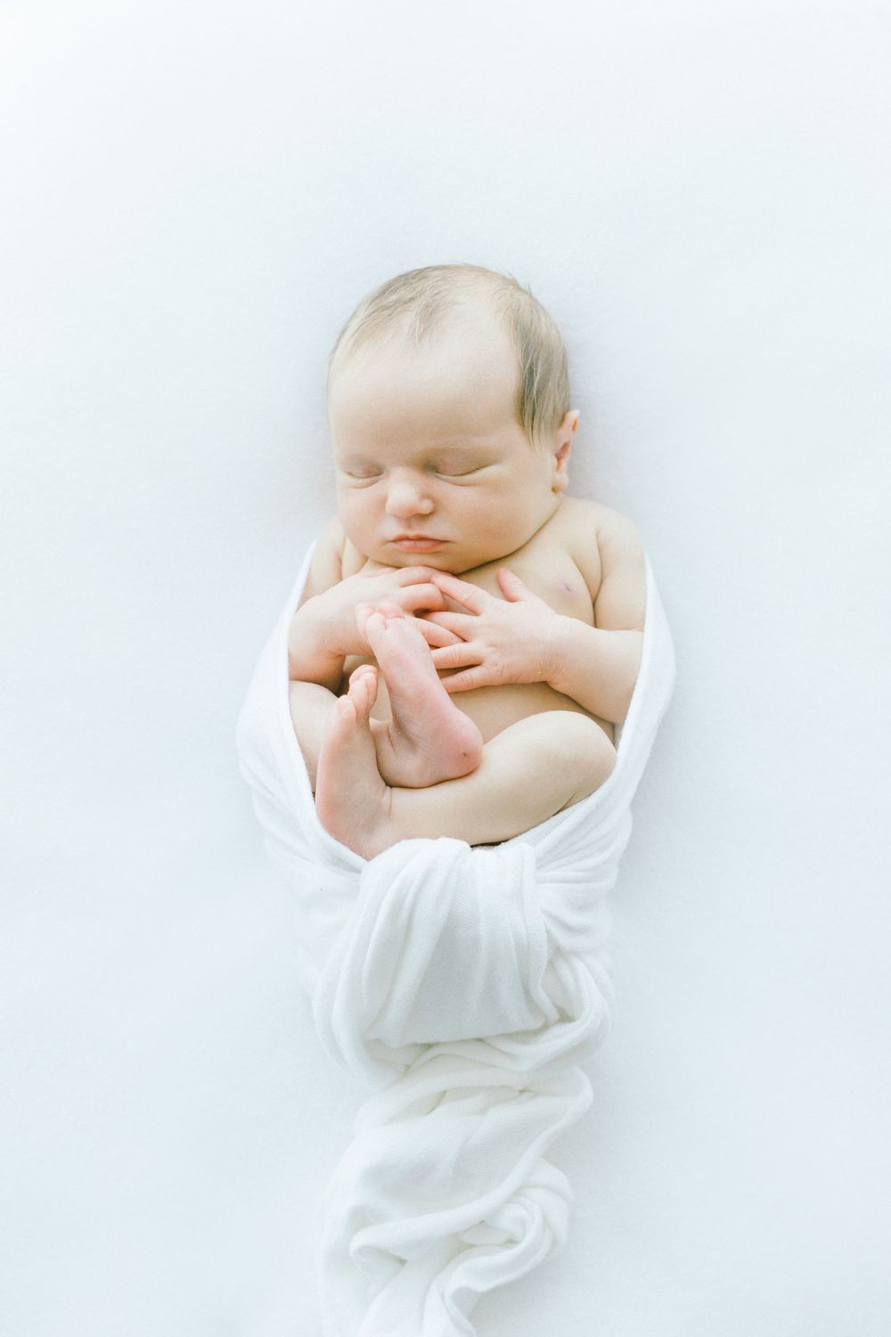 Infant wrapped in soft white fabric sleeping peacefully.