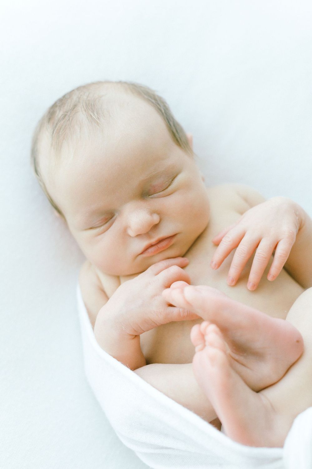 Tender close-up of sleeping baby wrapped in white.