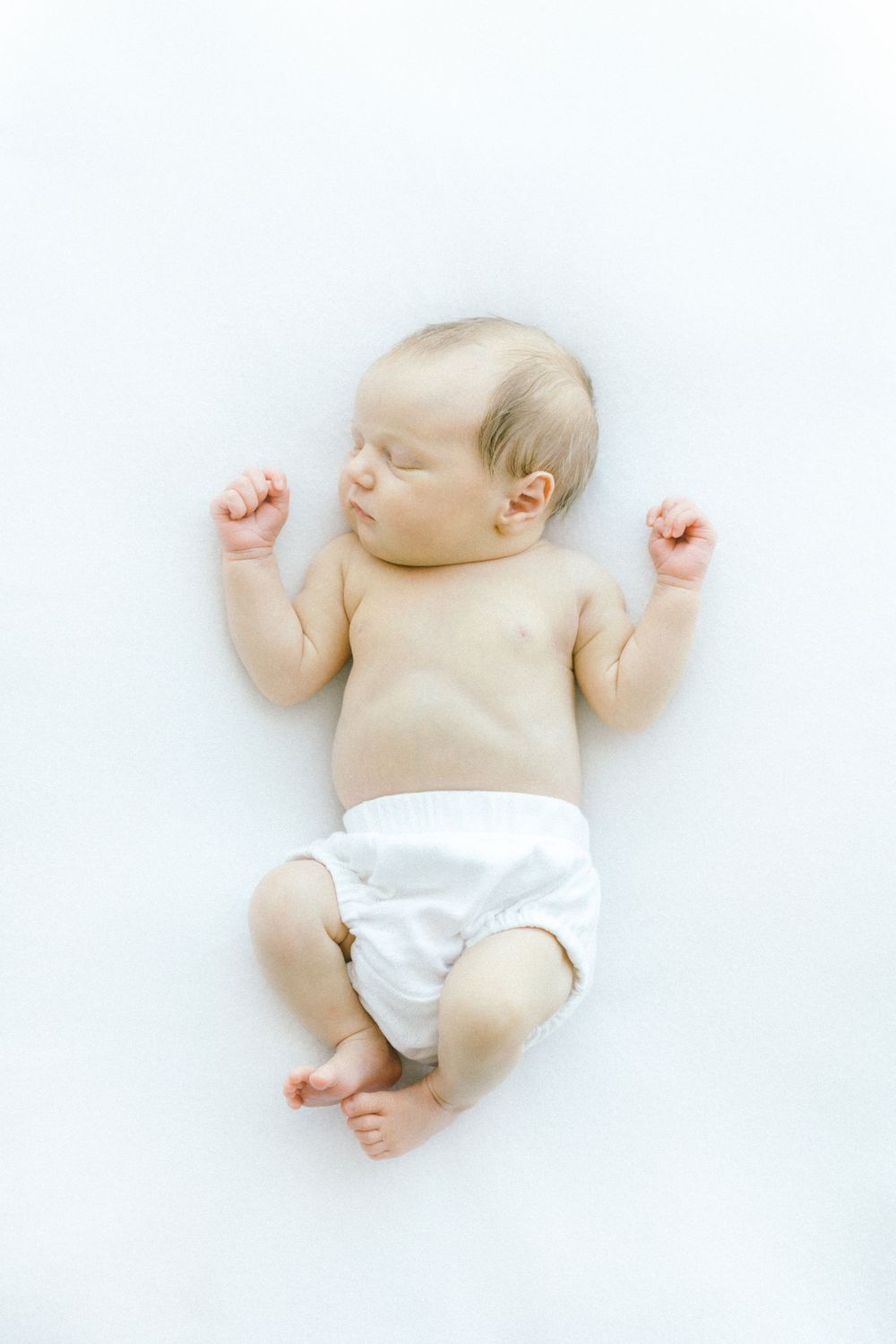 Newborn baby wearing white diaper sleeping on light background.