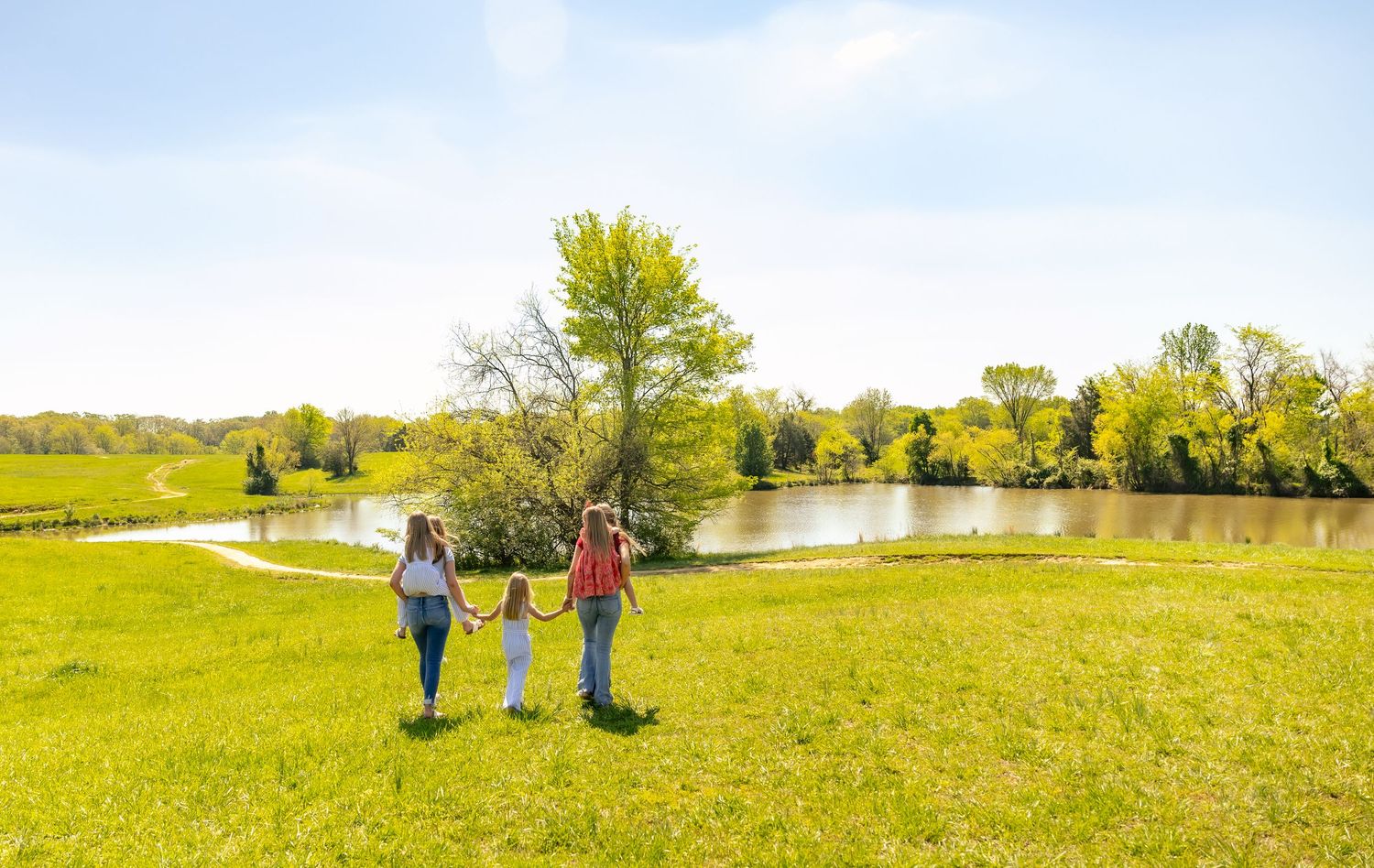 A group carries their bags while walking through a grassy field on a sunny summer day.
