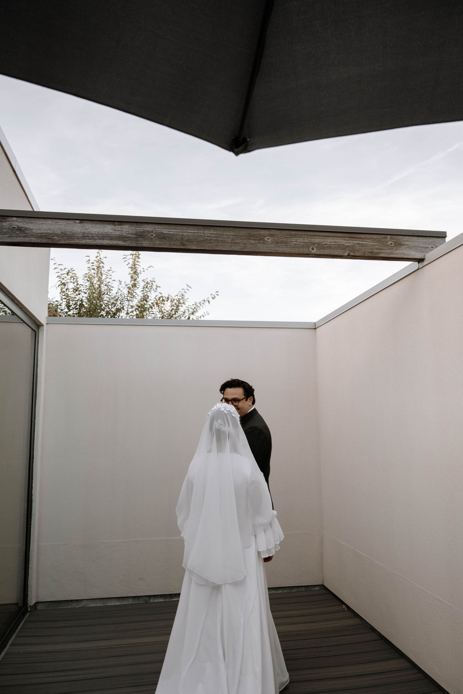 A couple shares an intimate moment on a rooftop terrace with white walls and a black umbrella overhead.